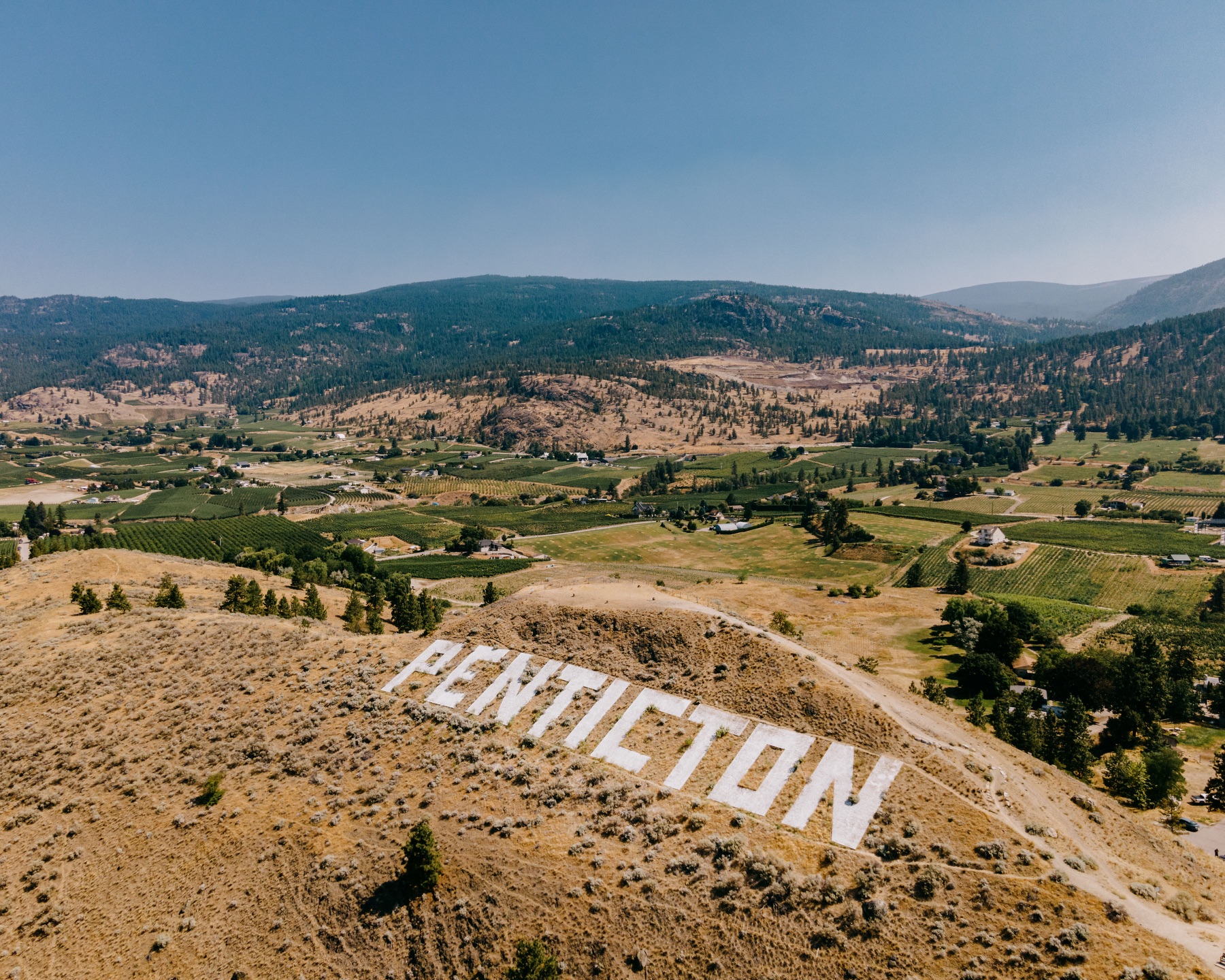 Aerial view of the Penticton sign overlooking vineyards and hills.